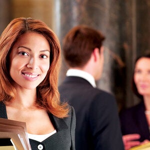 Professional in a suit holding a stack of file folders, with similar people behind them talking