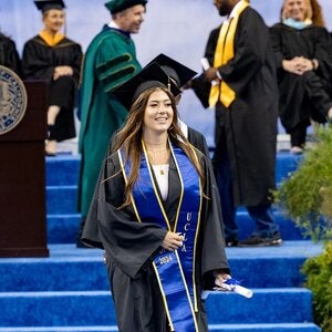 graduate walking on blue carpet with the stage in the background