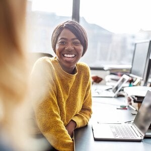 woman wearing a yellow sweater smiling at her desk